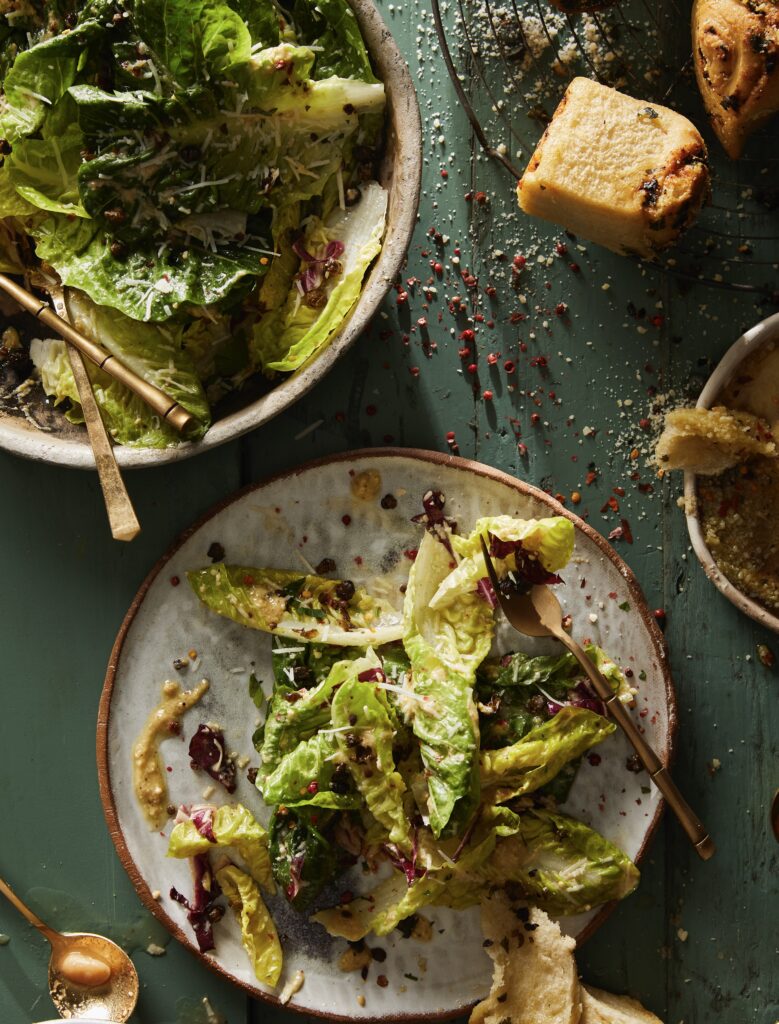 Two plates of caesar salad with seasonings all over on a green table.