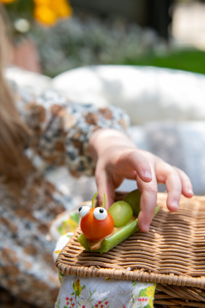 A kid plays with an edible bug made of celery and grapes.