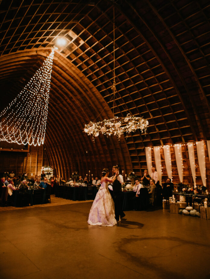 bride and groom dance in rustic ball room with fairy lights