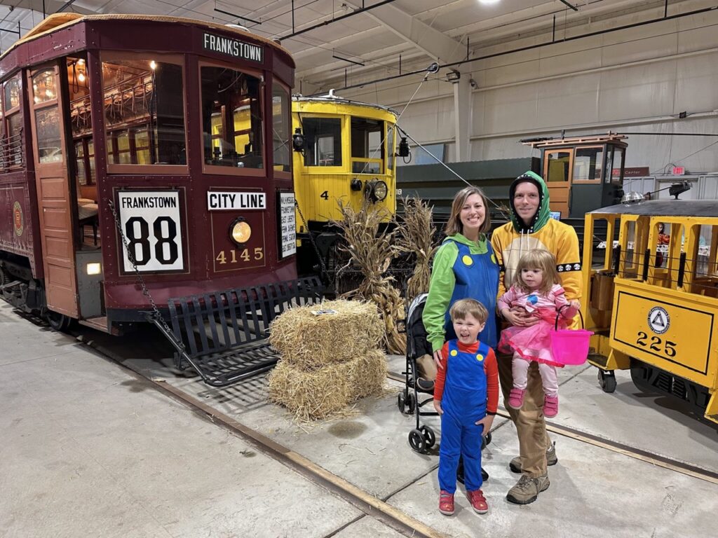 Family dressed as Mario characters at Pittsburgh Halloween event with vintage train.