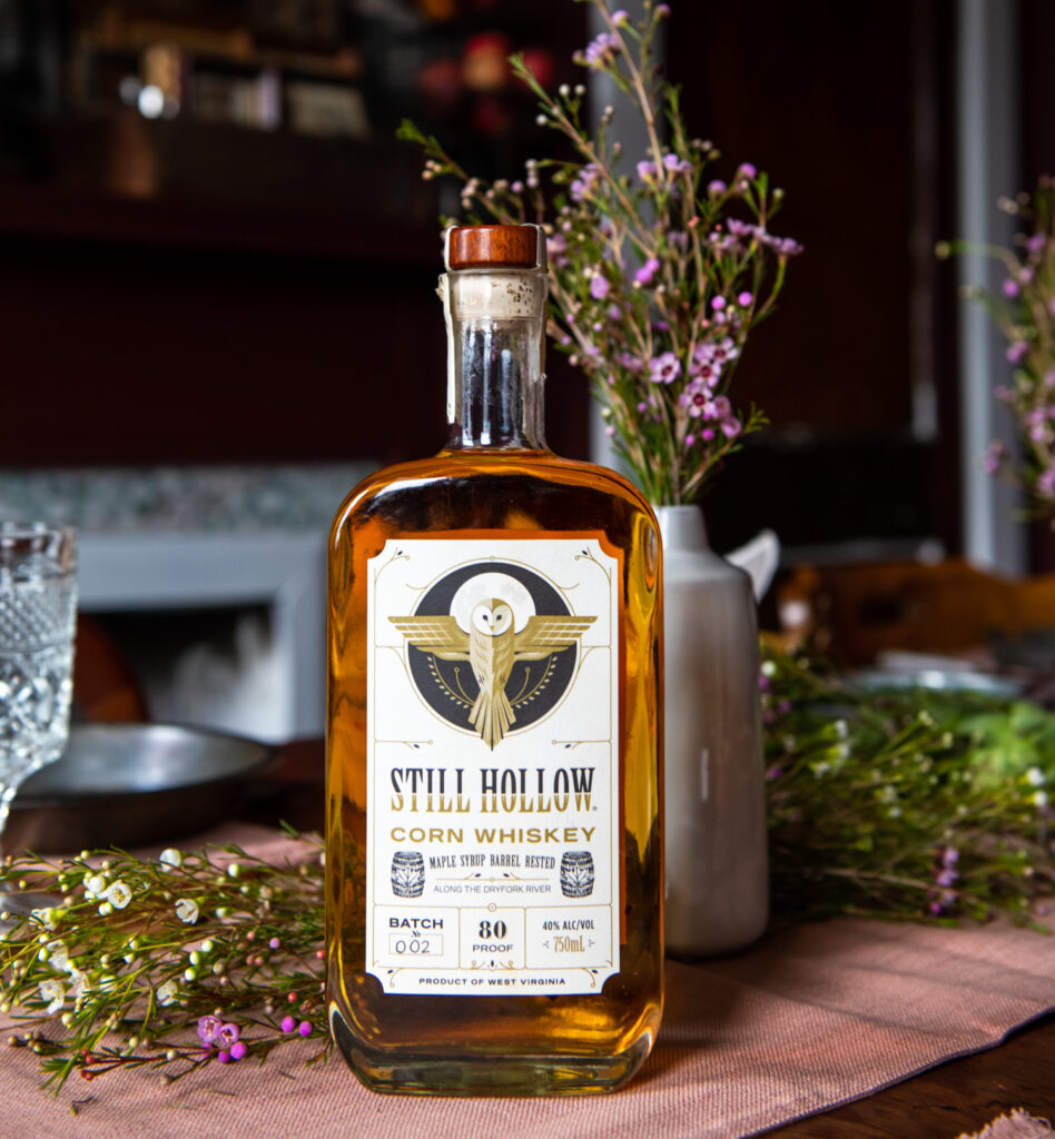 An amber bottle of corn whiskey on a picnic table with flowers. 