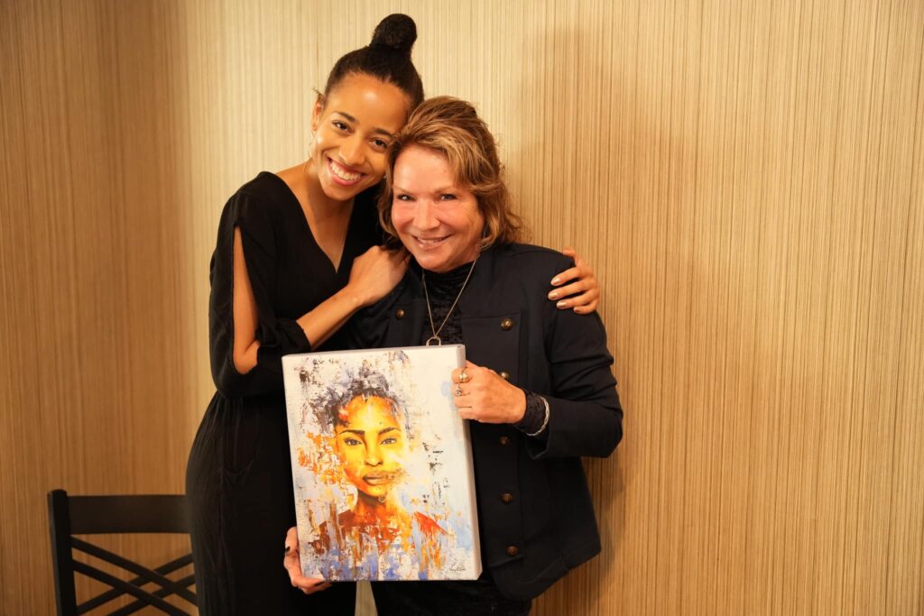 Art & Soul: Of the African American Woman two women hugging holding a painting.