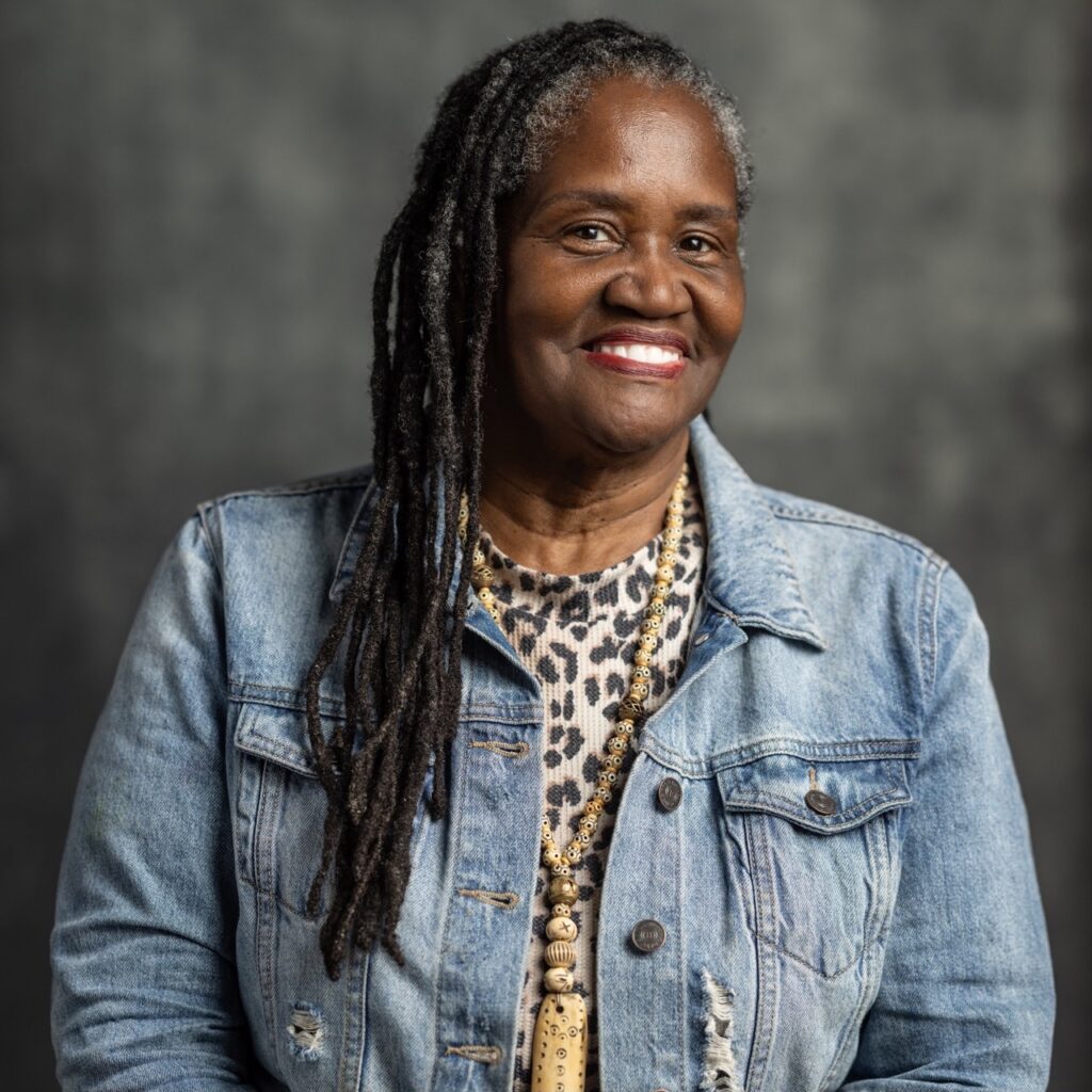 A woman in a jean jacket sits against a grey photo backdrop.