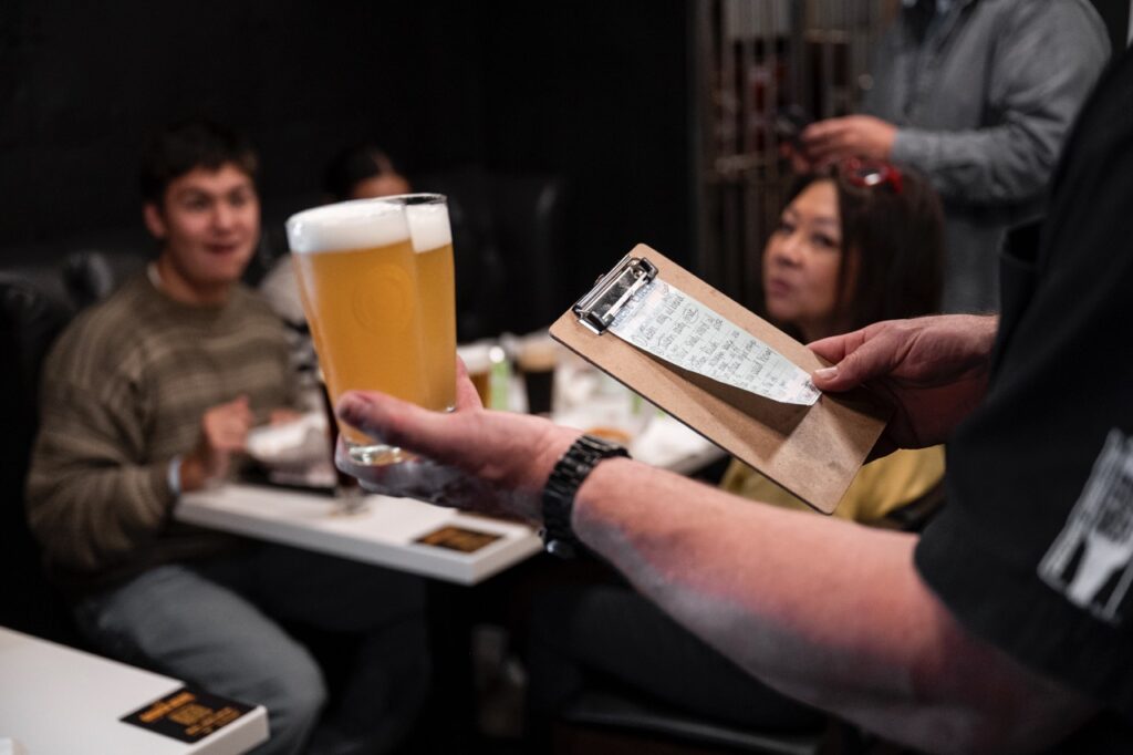 A man holds two beers and a menu in his other hand.