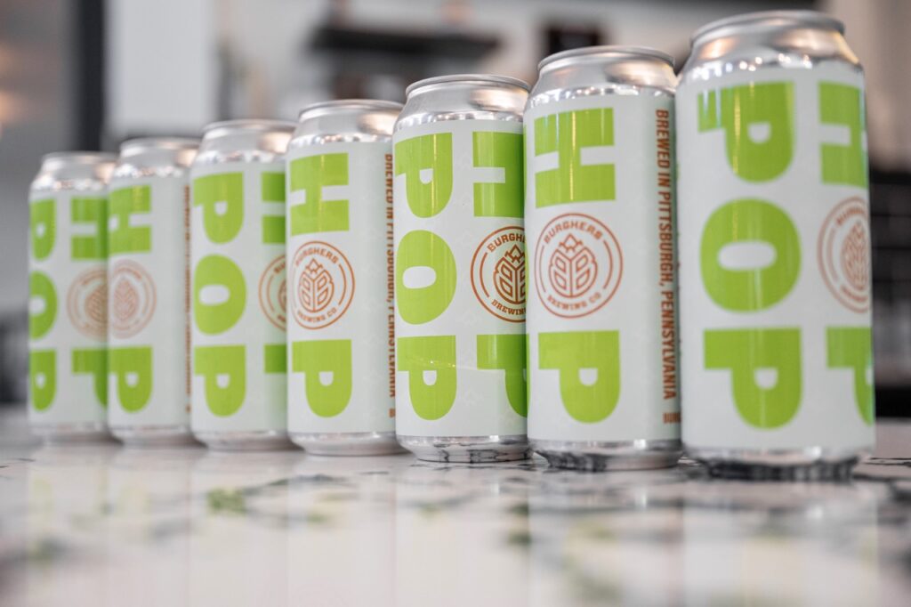 A line of craft beer cans in white with green letters on a marble counter.