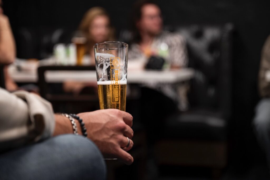 A man holds a half drunken beer in his hand.