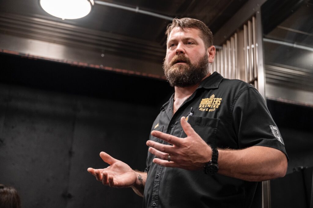 A man in a black shirt stands and explains in a room.