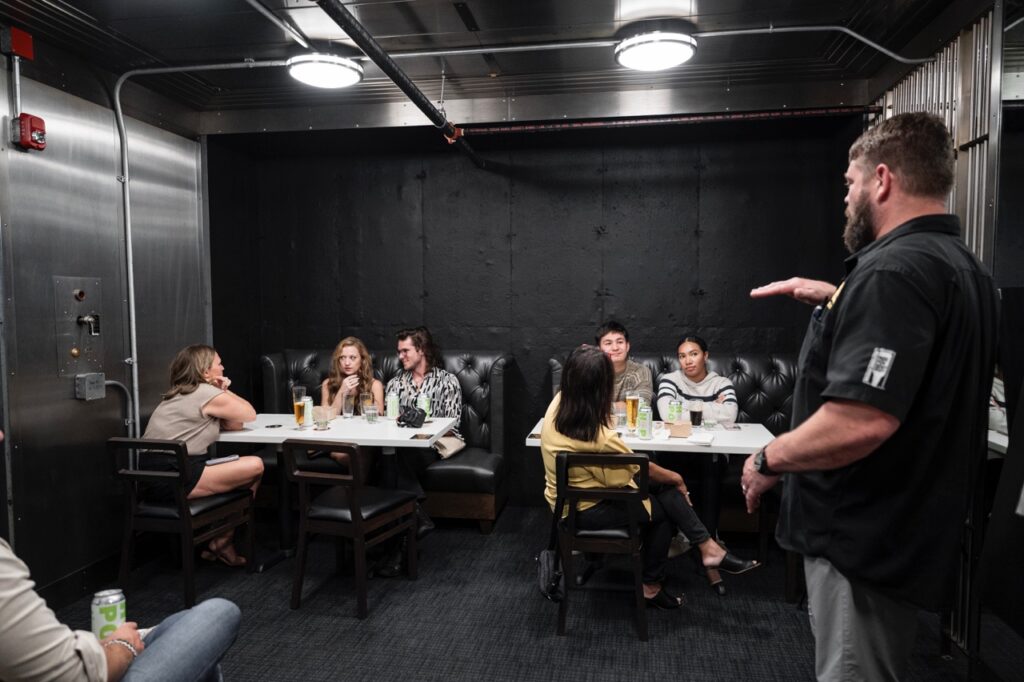 Two tables of beer tasters in a silver and dark room.
