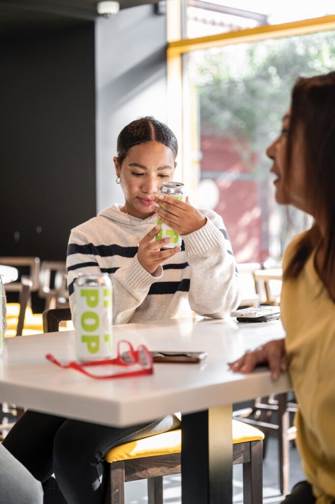 A woman looks at a beer can with neon green letters.