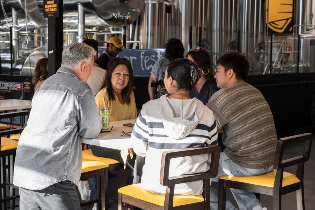 Four people talk at a yellow table in the sunshine.