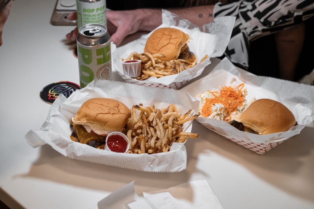 Three baskets of burgers on a table beside cans of craft beer.