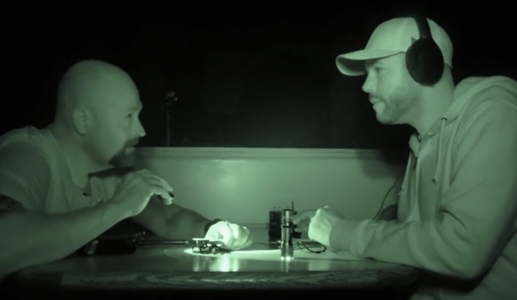 Two ghost hunters sit at a table in nightvision lighting.