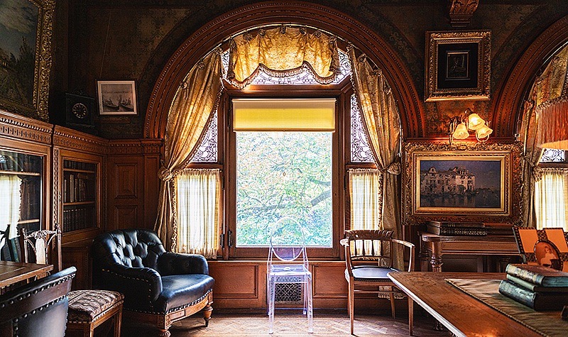 The inside of The Frick Clayton Mansion with antique wood furniture and a large window.