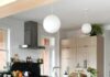 Renovating a 120-year-old Highland Park Kitchen A bright, modern kitchen featuring a large black marble kitchen island with white veining, light wood cabinets, and six industrial-style olive green barstools beneath two large white globe pendant lights.