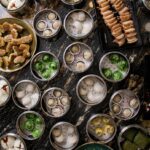 A variety of dumplings placed in round silver pans fill up a large dining table.