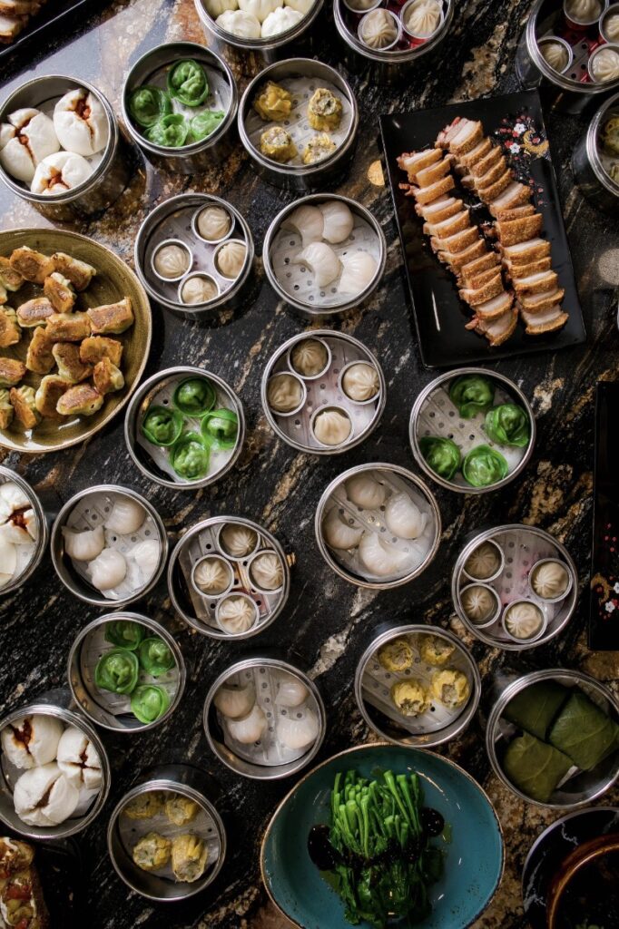 A variety of dumplings placed in round silver pans fill up a large dining table.
