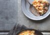 Easy as Shepherd’s Pie A cast iron skillet filled with Shepherd's pie topped with a golden-brown, bubbly rutabaga and potato mash, with a serving on a small gray plate.