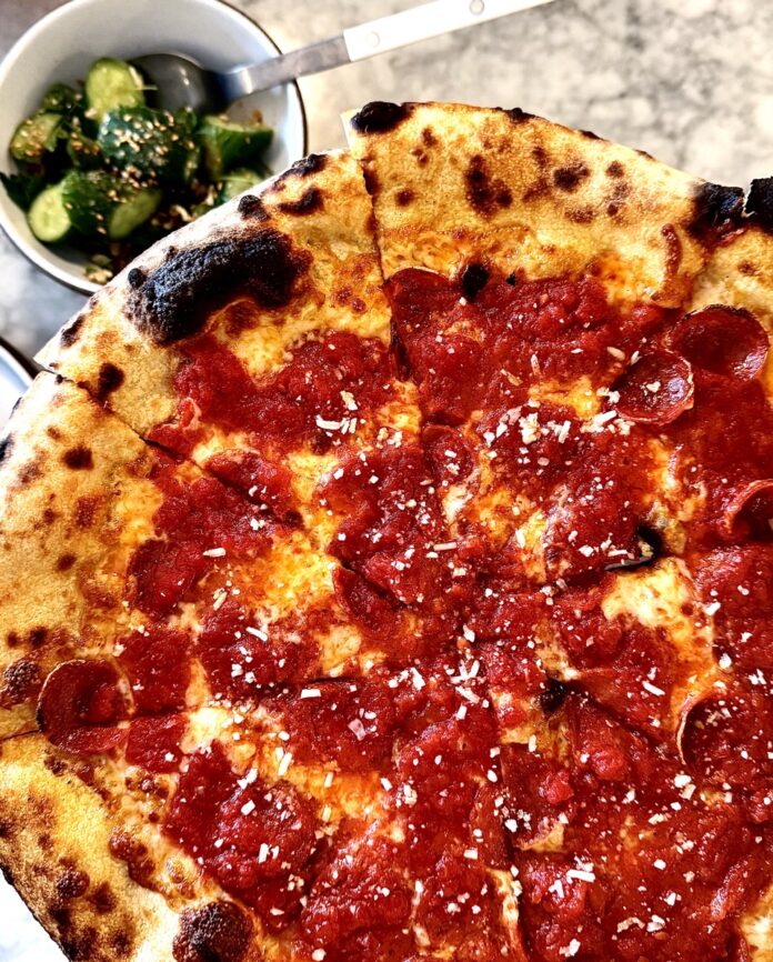 A pepperoni pizza with a bowl of cucumbers below it from F&F Pizzeria in Pittsburgh.