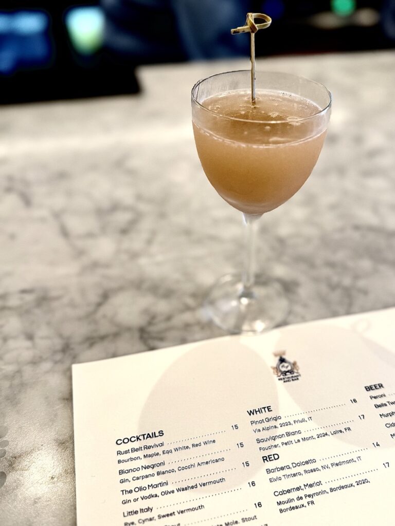 A cocktail glass with a toothpick in it on top of an F&F Pizzeria menu.