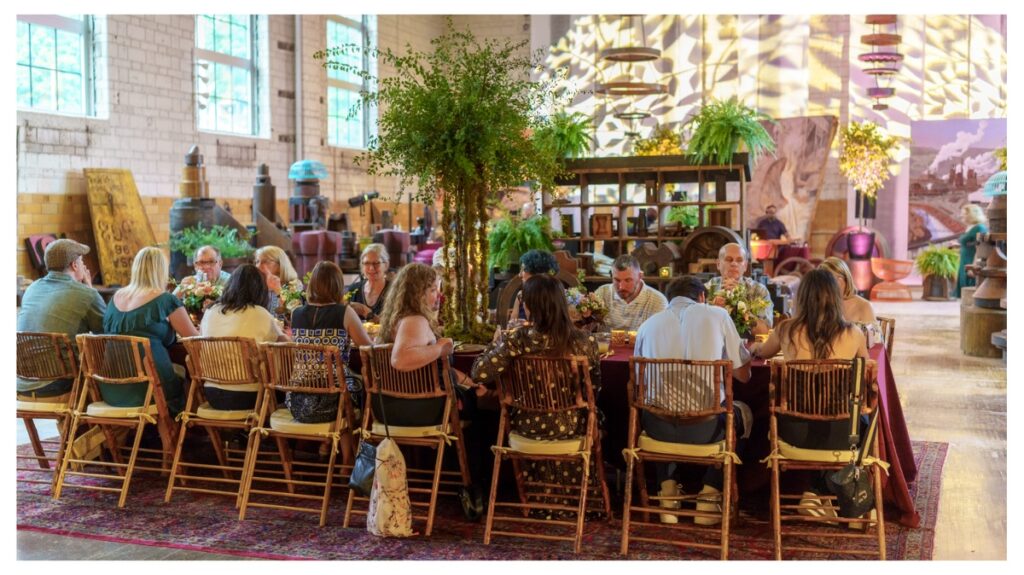Guests seated at a long, low table with bamboo chairs and a rich red tablecloth enjoying the Moroccan-themed party dinner at Cory Bonnet Studio.