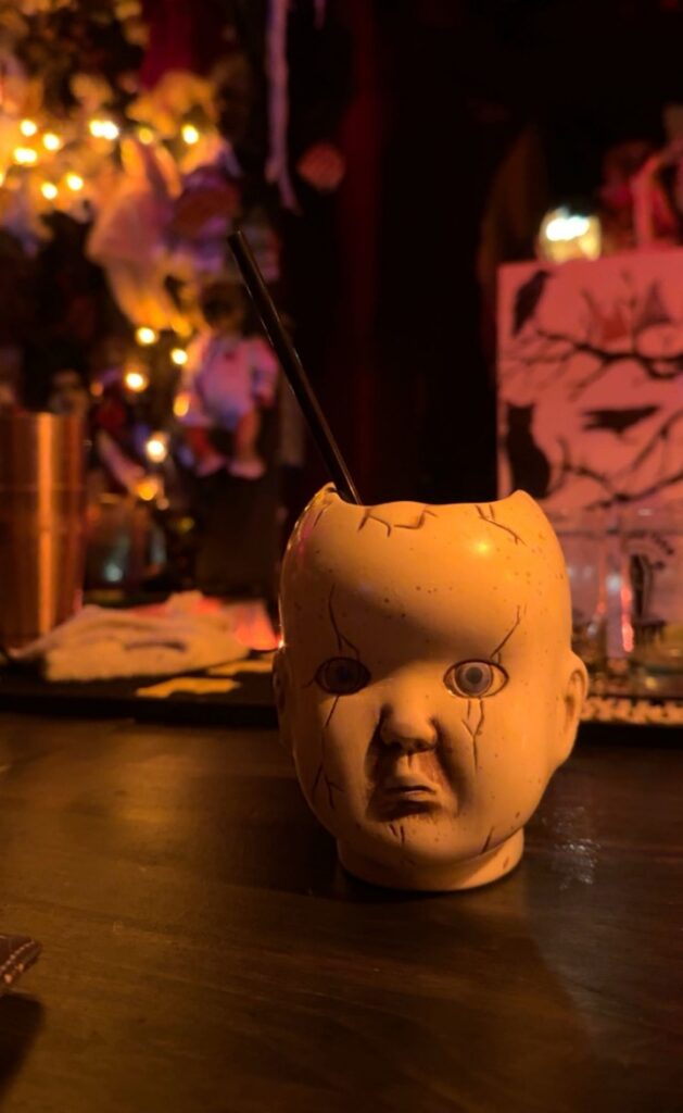 Creepy doll head cocktail at a Pittsburgh Halloween bar, with spooky decor.