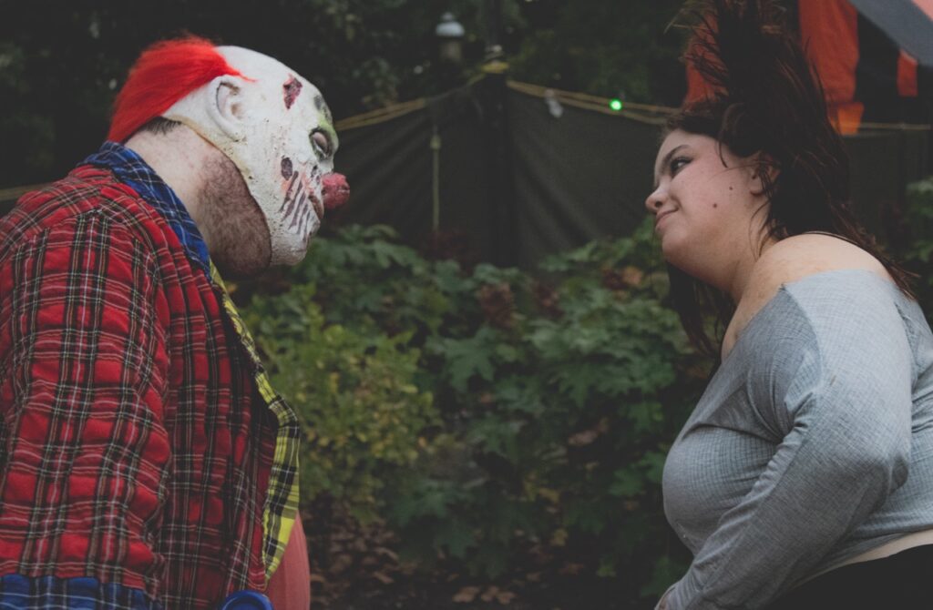 A clown and a woman dance together.