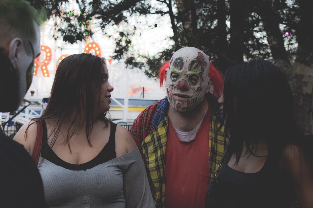 A person in a decaying clown mask between two girls.