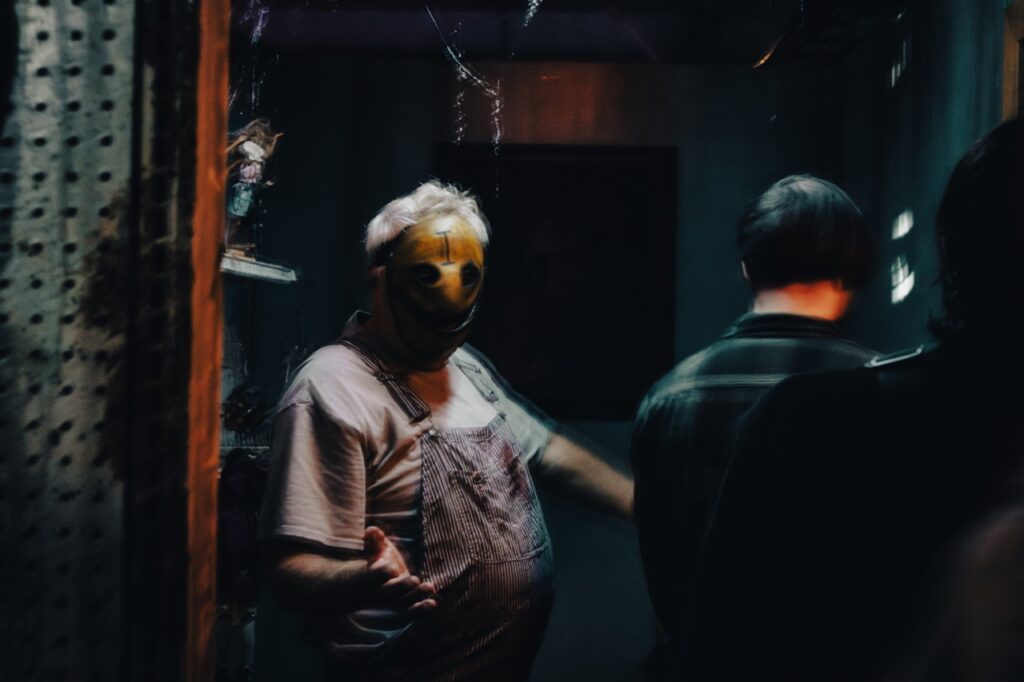 A man in a creepy mask directs a group through.