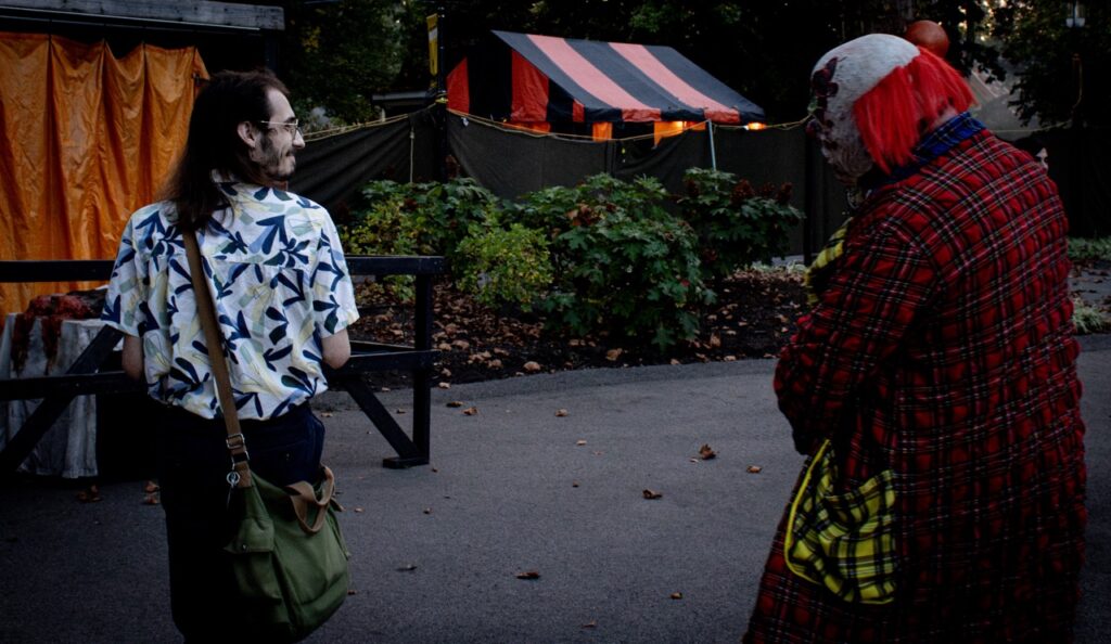 A man looks over at a clown costume man.