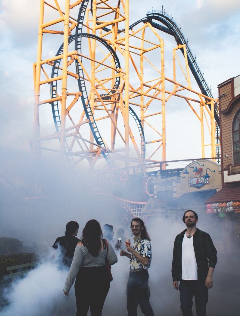 A group of park goers at Kennywood walk through thick fog in front of a roller coaster.