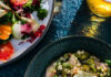 Warm Up the Soul with These 25 Soup Recipes A bowl of soup with little round noodle balls, greens, chicken, and lemon slices on top sits in a dark teal bowl with a winter citrus salad sitting nearby.