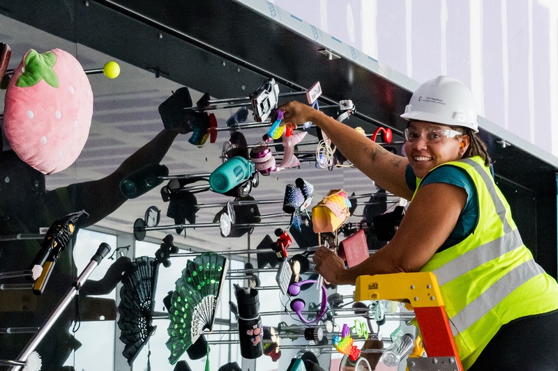 A woman puts up materials against a wall for an art piece in Pittsburgh Airport.