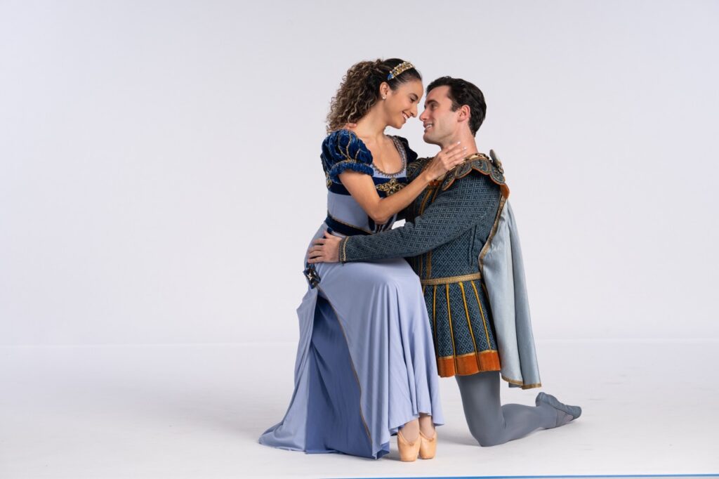 A ballet dancer in a long dress sits on a man's knee.
