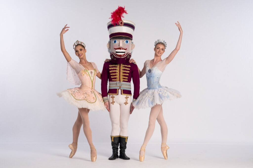 Two ballet dancers stand on either sides of a Nutcracker dancer.