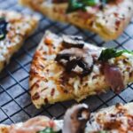 A slice of Prosciutto, Mushroom, and Spinach White Pizza cooling on a wire rack.