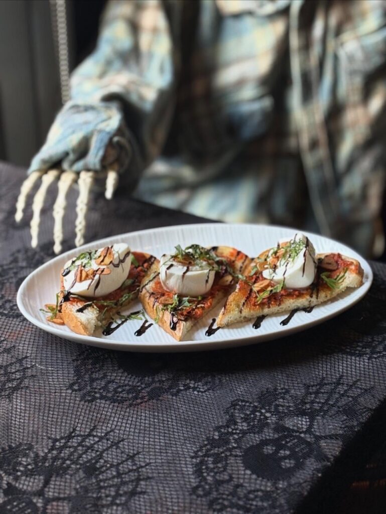 A plate of eggs and toast on a Halloween table cloth with a skeleton behind it.