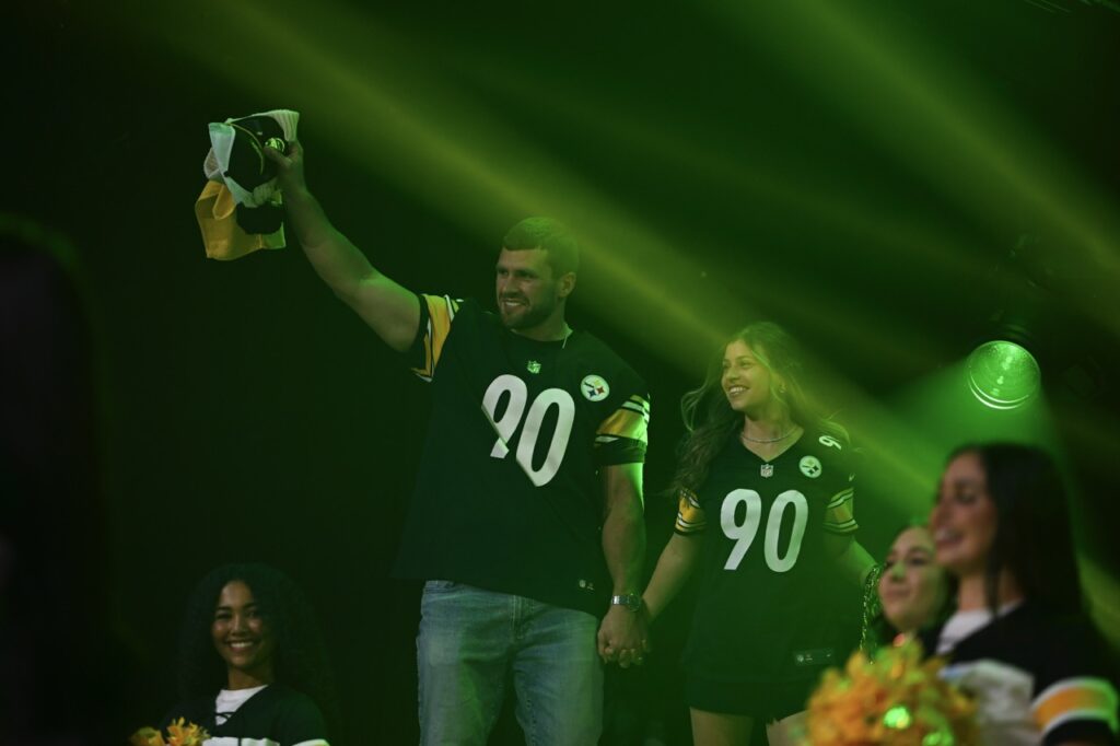 A man and woman in Steelers jerseys on stage in green lighting.