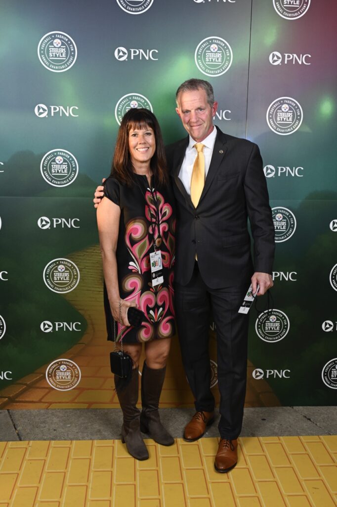 A man in a black suit and yellow tie stands with a woman in a black and pink dress.