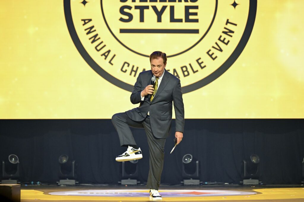 A man shows off black and gold Nike shoes with a suit and tie on a stage.