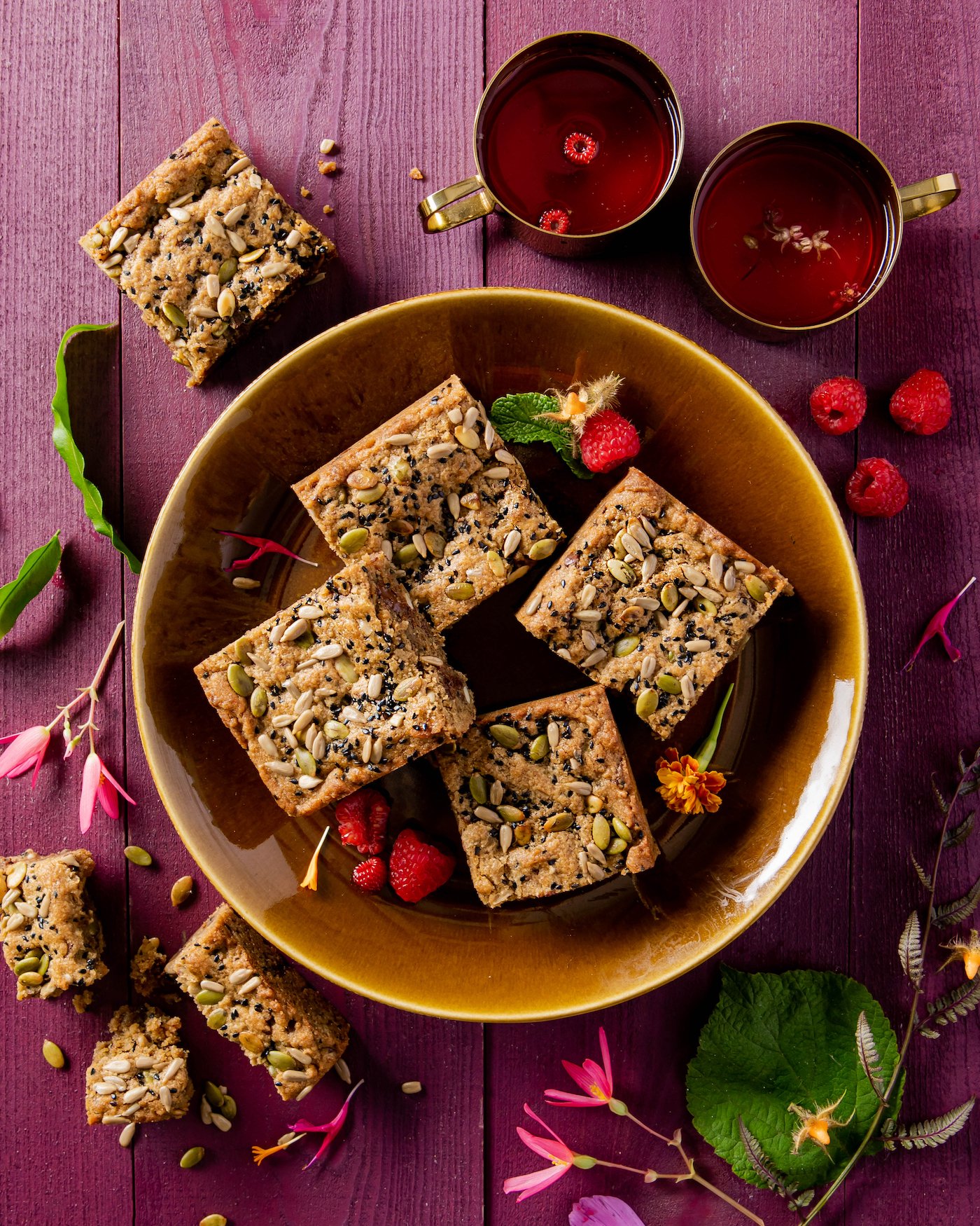 Four SunButter® Blondies sit in a brown bowl with raspberries sprinkled around the desserts.