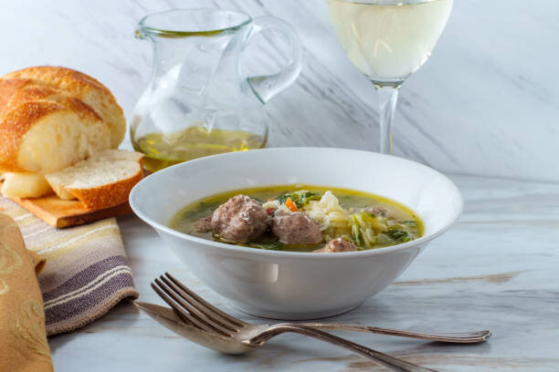 Vegetarian Italian Wedding Soup in a bowl with a fork and spoon and slices of bread on the side