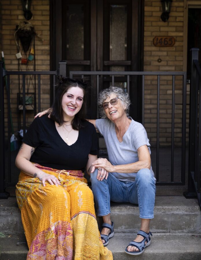 An older woman sits on the stairs with her arm around the shoulders of a younger woman.