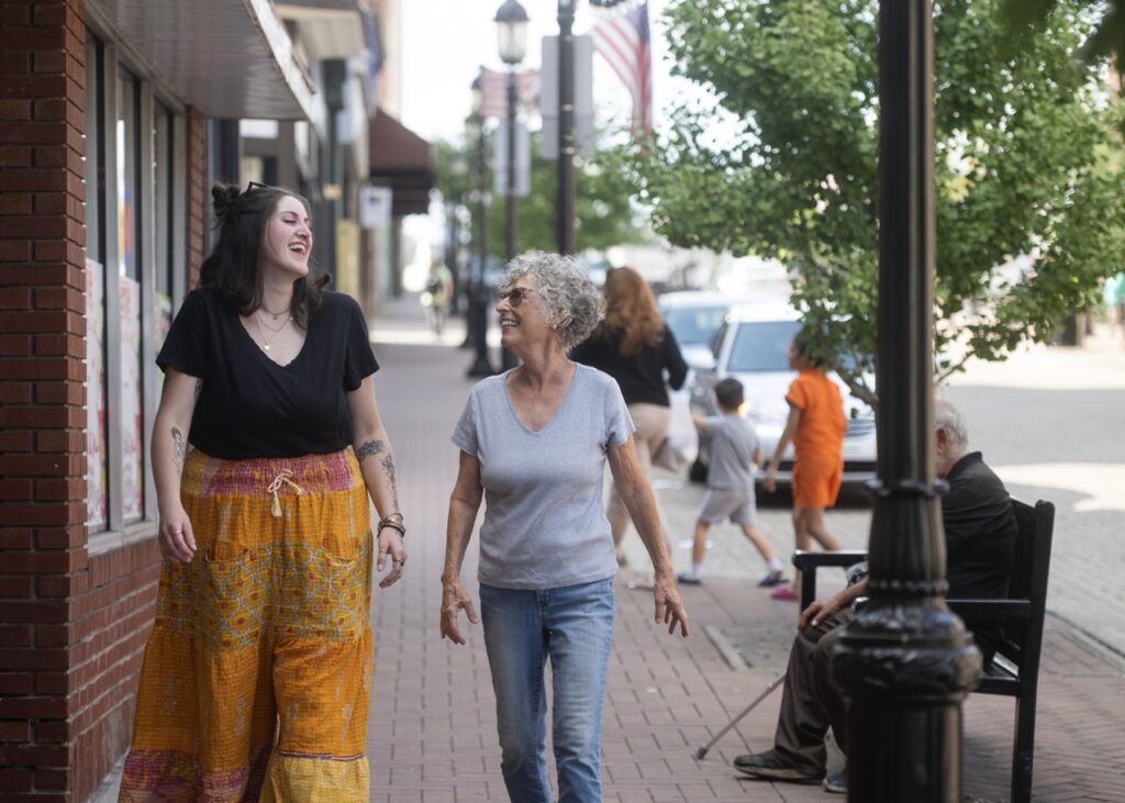 A young woman and an older woman walk down a brick sidewalk together.
