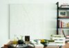 Weisshouse Owner Cyd Mello Talks Turning a Pittsburgh Storefront Into a Home A modern dining area featuring a light wood rectangular table, black spindle chairs, and a black metal and glass shelving unit displaying woven baskets and decor, contrasting against white walls.