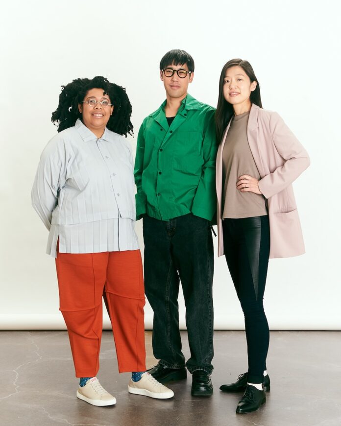 Three art curators stand against a white wall in a group.