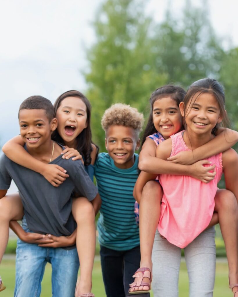 Two children give two other kids piggy back rides as another child stands between them.