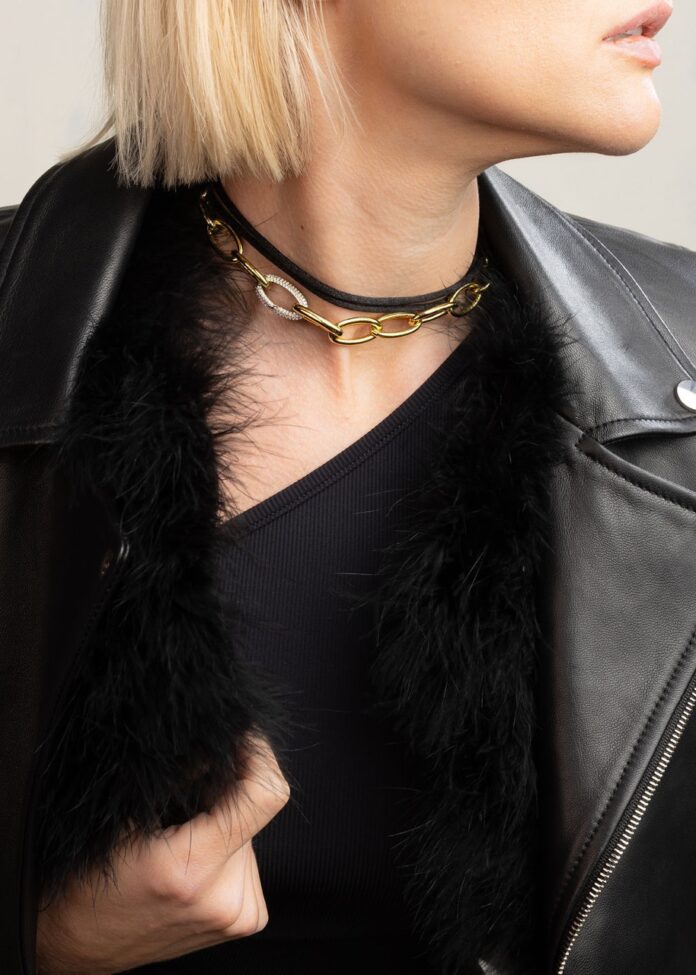 A woman wears a black shirt and jacket with a gold chain necklace.