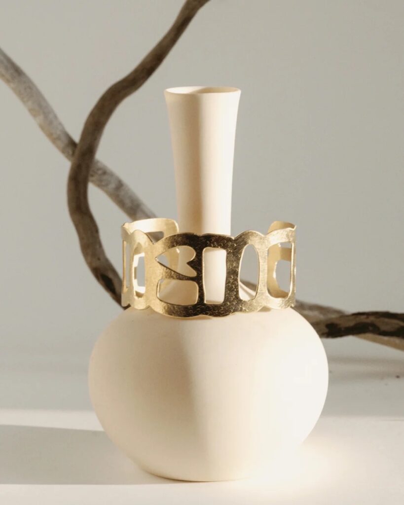 A gold structured jewelry cuff on a white bracelet stand.