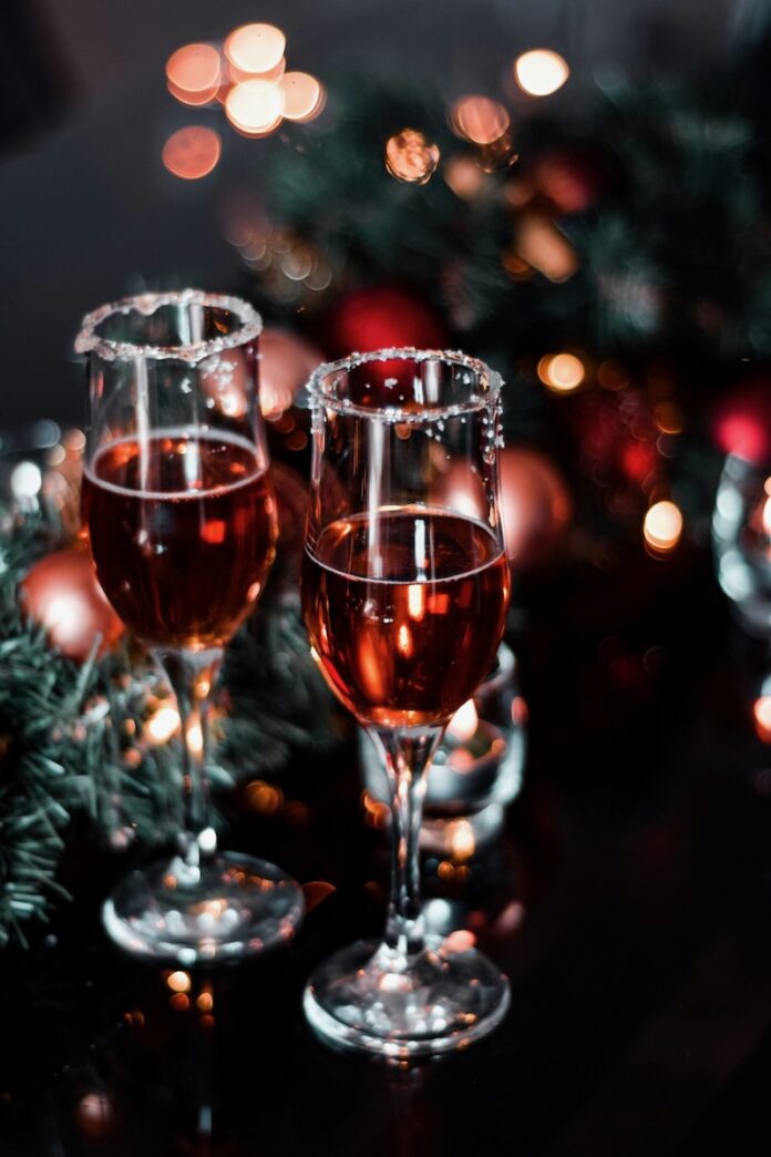 The Best Wines for Your Holiday Dinner Table Two champagne flutes with red wine on a holiday table with lights and bulbs.