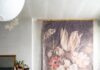 Using the KonMari Method as a Fresh Start for Home Design A woman, Quelcy Kogel, in a long floral dress sits with a coffee cup next to a large, faded floral tapestry and a sleeping black and white dog on a magenta cushion in a rustic, minimalist living room.